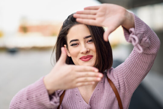 Portrait of smiling young woman shaping frame with her hands