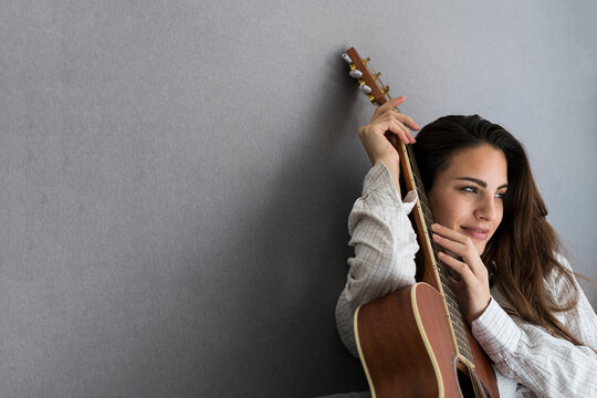 Portrait of smiling young woman with guitar in front of grey background