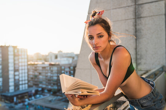 Portrait of young woman wearing bra reading book on balcony
