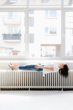 Woman lying on heater in front of window