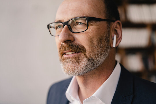 Portrait of mature businessman listening to music with bluetooth earbuds