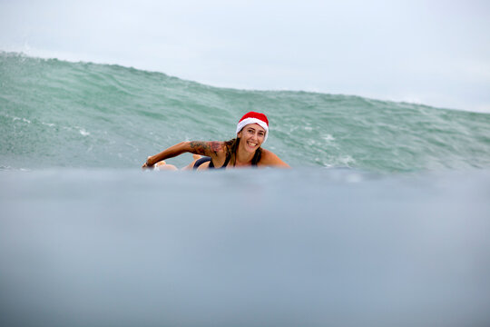 Indonesia, Bali, smiling woman on surfboard wearing Santa hat