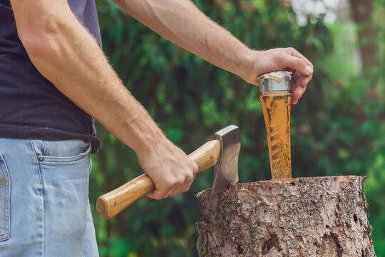 Man standing at a tree trunk holding an axe and a wedge