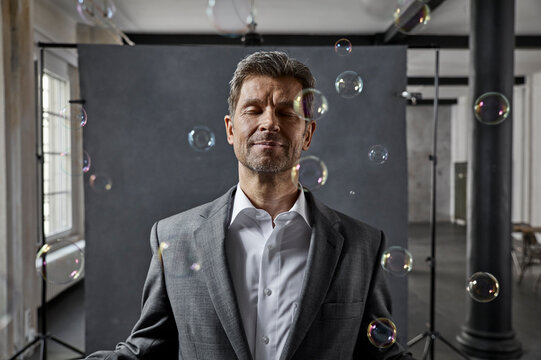 Portrait of mature businessman with bubbles in front of black backdrop in loft