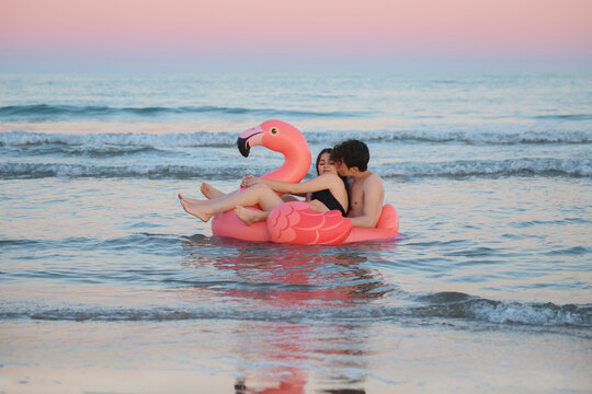 Couple in love floating with inflatable pink flamingo on the sea at sunset