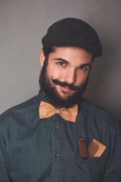 Portrait of bearded man wearing cap, denim shirt, cork bow tie, wearing wooden combs for beard and mustache in his pocket