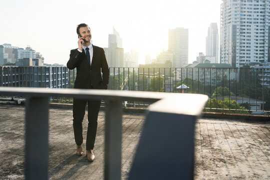 Business man in dark suit speaking into smartphone on city rooftop