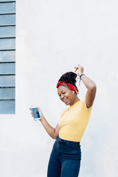Young woman listening music with headphones and earphones singing and dancing in front of white wall