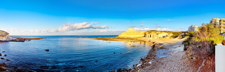 Panorama with pebble beach, rocks, buildings and blue sky at Zebbug on the island of Gozo, Malta © EKH-Pictures