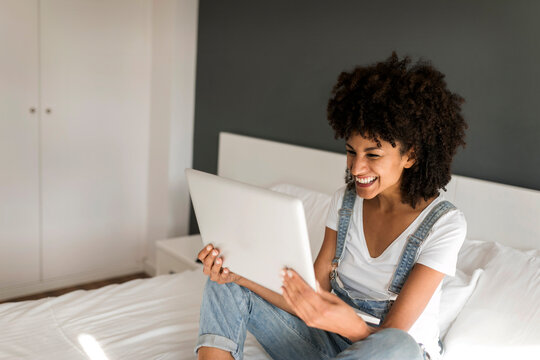 Happy woman sitting on bed looking at tablet