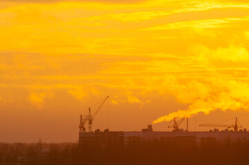 Fototapeta premium Construction cranes silhouettes over the construction site of the panel residential houses, industrial sunset view of construction works in winter