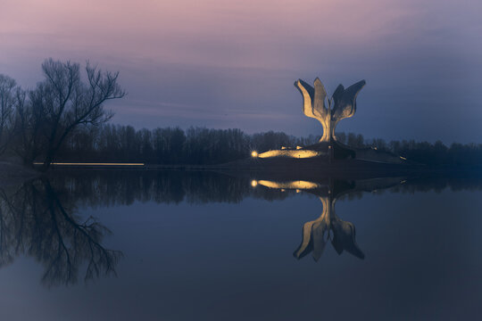 View of the Stone Flower monument reflecting in the still waters under a dusky sky, a serene yet somber scene, Jasenovac, Sisak-Moslavina County, Croatia.