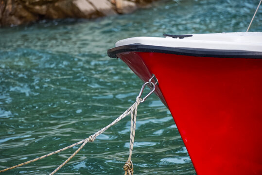 Close up of a red boat bow secured with a rope and metal carabiner on turquoise sea water during summer vacation travel for nautical transport and maritime lifestyle in Croatia.