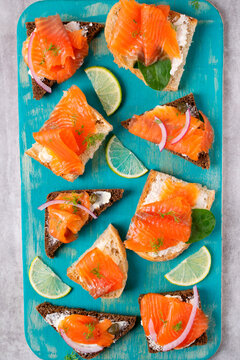 Bruschetta set with smoked trout slices, cream cheese, red onion and capers on wheat and rye bread. Flat lay with appetizers on blue board. Top view
