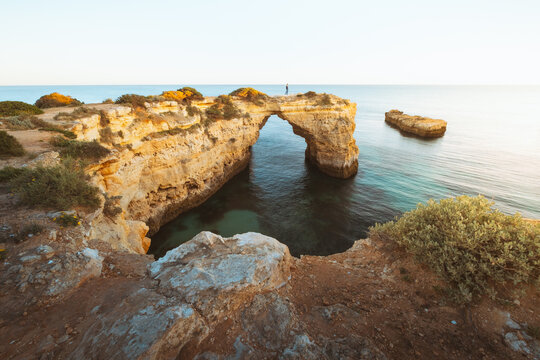 View of a mesmerizing natural arch carved by the sea's embrace, standing proudly against the sky, where golden cliffs meet the turquoise waters, Porches, Faro, Portugal.