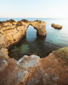 View of sun-kissed cliffs meet the turquoise sea, framing a natural archway over crystal waters, a coastal symphony of light and stone, Porches, Faro, Portugal.