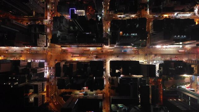 Asia world cities at night - overhead forward drone flight of illuminated streets, residential flats, and commercial office towers in Kowloon district of Hong Kong