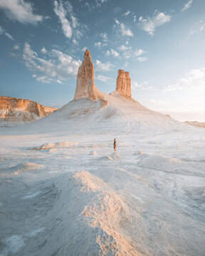 View of a solitary figure against the stark white landscape, framed by towering rock formations under a serene sky, Aktau, Mangystau Region, Kazakhstan.