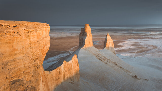 View of towering sandstone formations bathed in the warm glow of the setting sun against a stark, flat expanse, creating a surreal landscape, Aktau, Mangystau Region, Kazakhstan.