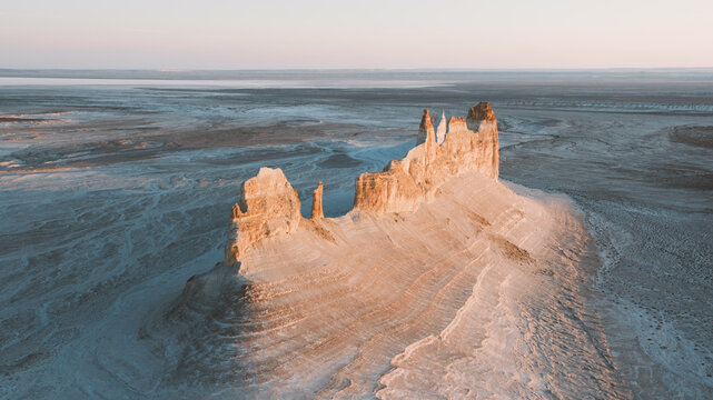 View of a majestic limestone mountain bathed in the warm glow of sunset, rising dramatically from the vast, textured plains, Aktau, Mangystau Region, Kazakhstan.