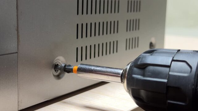 An electric screwdriver turns a screw into the metal chassis of the video player. As the threads tighten or loosen against the casing, they create a high-pitched, piercing metallic squeal.