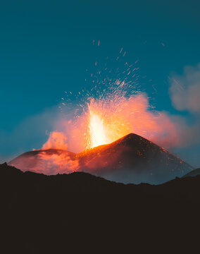 View of fiery volcanic eruption against the dusky sky, casting an orange glow over the dark silhouette of the mountain, Nicolosi, Sicily, Italy.