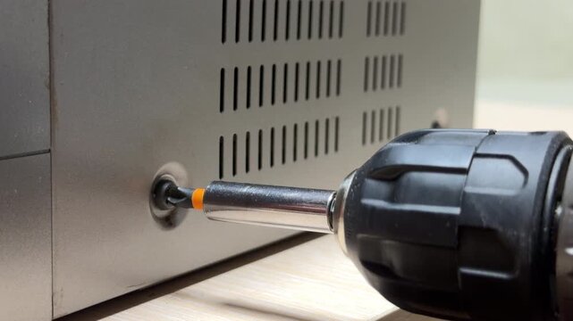 The electric screwdriver forces a screw into the metal casing with intense torque. This action creates a piercing, high-pitched metallic squeal followed by a sudden, jarring mechanical rattle.