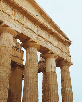 View of weathered stone columns reach skyward, remnants of ancient grandeur against a pale sky, whispering tales of time, Agrigento, Sicily, Italy.