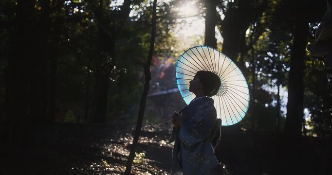 Japanese woman in kimono holding umbrella and turning around in forest - cinematic, silhouette, slow motion shot