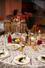 Fototapeta premium Beautifully arranged dinner table with assorted appetizers, fruits, salads, wine bottles, and candles in warm ambient lighting. Decorative centerpiece and elegant tableware create a festive atmosphere