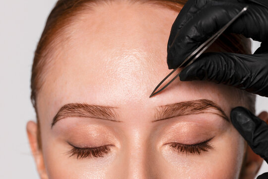 Professional brow shaping takes place at a beauty salon with an expert using tools on a client