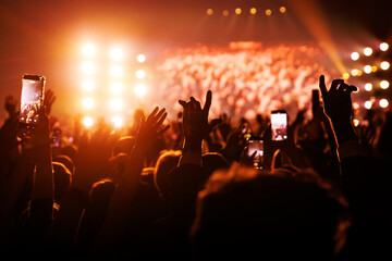 Music festival crowd with raised hands and smartphones under orange lights