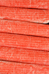 A detailed macro shot shows the red and white textured surface of several surimi crab sticks arranged horizontally next to each other.