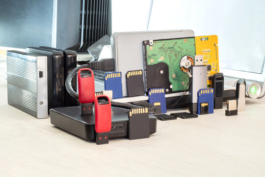 A collection of USB flash drives, memory cards, and external hard drives against a laptop. A showcase of computer accessories for data storage and backup