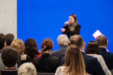 Obraz premium Audience watches a speaker on stage against blue backdrop, presentation in progress, professional setting