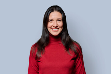 Fototapeta premium Portrait of beautiful smiling 40 years old woman posing on light gray background