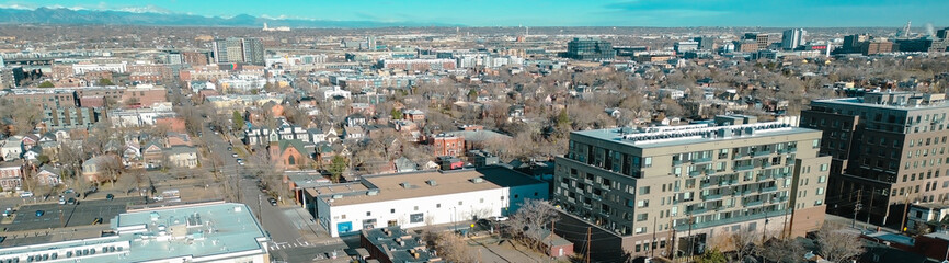 Panorama aerial view neighborhood blocks near Curtis Park extend toward high rise clusters along Champa St. Clear skies brighten varied roofs HVAC units, brick tones, seasonal foliage, Denver, CO