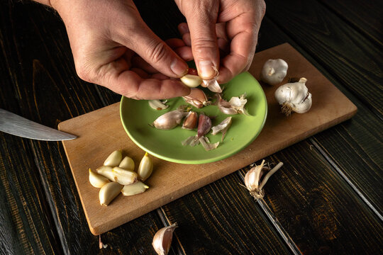 Hands preparing garlic cloves on a wooden cutting board in a kitchen setting during the day