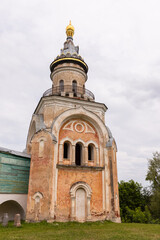 Fototapeta premium Historic Orthodox church tower with a golden dome and weathered plaster facade set against a cloudy sky, Boris and Gleb Monastery Novotorzhsky, Torzhok, Russia