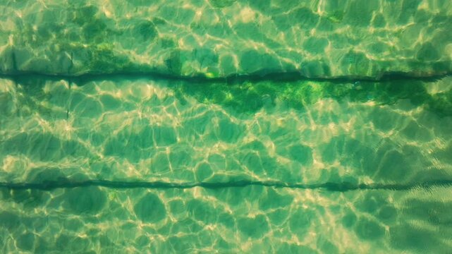 Close-up view of sunlight filtering through green water with ripples on the surface in a pool.