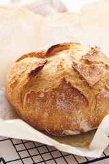 Round sourdough loaf resting on black wire cooling rack with beige linen towel. Perfect for baking, food blogs, and culinary projects