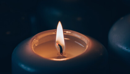 A lit candle with a flickering flame in a dark setting.
