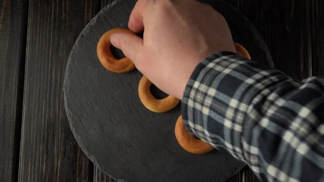 A hand arranges bagels on a black granite board before serving the dessert on a festive table.