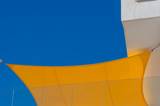 Abstract modern canopy membrane in yellow and blue creating shade and geometry against open sky with space for branding and summer events