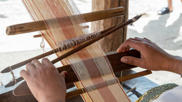 Hands weaving fabric on traditional wooden loom in rural workshop