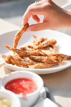 A person is eating fried fish with a dipping sauce