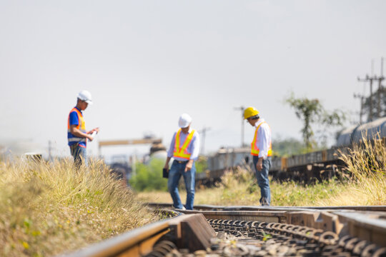 Close-up of railway tracks with a team of blurred engineers performing a safety inspection and maintenance check in the background, Professional civil engineers surveying a train track site