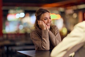 Smiling Woman In Cozy Brown Sweater Enjoys Conversation At A Warm Café