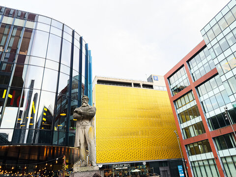 Manchester Gasworks plaza with modern glass buildings and Friedrich Engels statue in vibrant urban city center scene
