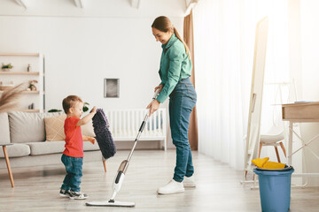 Let's tidy up together. Mother and kid son do the cleaning in the house. Little boy helping mom, giving her a rug while woman wash the floor with mop